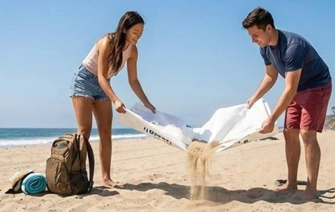 Two people shaking sand from lightweight Tyvek tent footprint ground cloth for camping and backpacking on a beach