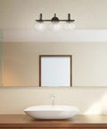 Lofty Chic Three Light Vanity Light In Dark Bronze With Clear Glass Shades And Antique Brass Accents for modern bathrooms