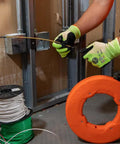 Hand holding a Top Shelf 13 Inch Flexible Fish Tape Leader for 1/8 Inch Steel Tapes, guiding wire through a wall cavity.
