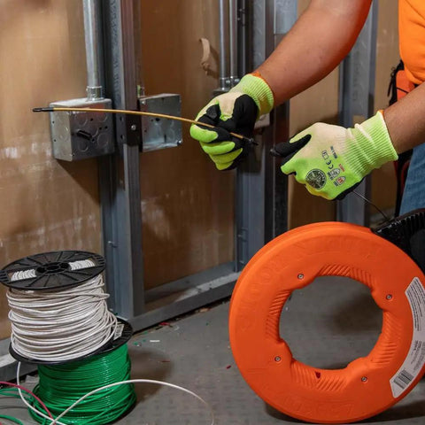 Hand holding a Top Shelf 13 Inch Flexible Fish Tape Leader for 1/8 Inch Steel Tapes, guiding wire through a wall cavity.