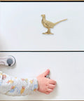 Top Shelf Brass Pheasant Drawer Knob With Rich Golden Finish on white cabinet, child’s hand pulling drawer handle.