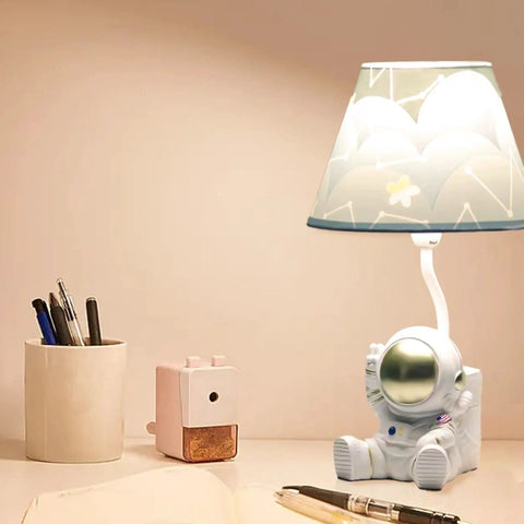 Golden Astronaut Kids Table Lamp With Barrel Lampshade, 13 Inch Spaceman Bedside Table Lamp, on desk with stationery.