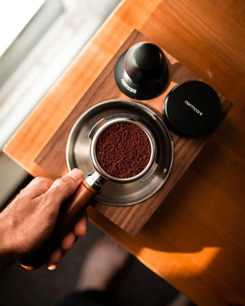 Hand holding portafilter with grounds next to 58mm Coffee Distribution Tool For Espresso Portafilter Leveler With Adjustable Depth And Stainless Steel Base Barista Leveling Stand For Even Grounds And Consistent Tamp Go To Accessory For Home Coffee Enthusiasts