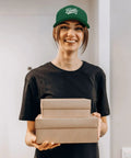 Woman wearing Cool Uncle Club EST 2026 Like A Dad But Cooler Green Trucker Hat holding gift boxes