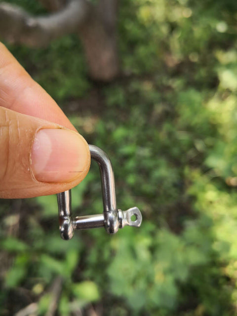 Close-up of Stainless Steel Mini D Shackle 4mm For Paracord Jewelry And Everyday Outdoor Gear held between fingers outdoors.