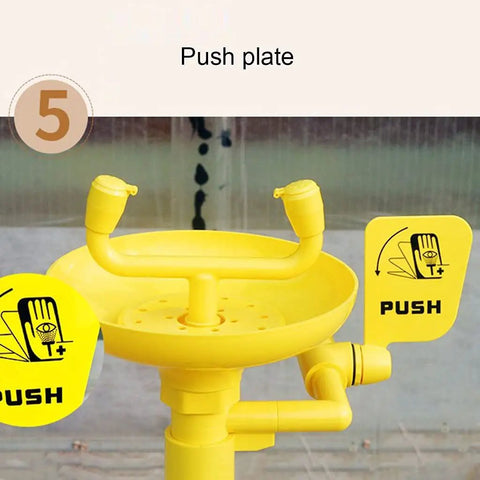 Close-up of yellow push plate on stainless steel 304 emergency eyewash station floor mounted with dual nozzles.