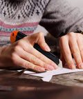 REXBETI retractable utility knife with orange cap and black handle cutting paper.