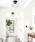 Industrial Semi Flush Mount Ceiling Light With Seeded Glass Shade installed in a modern white hallway with plants and a mirror.