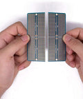 Hands holding two halves of a Four Piece Solderable Breadboard Shield With Split Design PCB Prototyping Board Double Sided Tinned Gold Plated Holes.