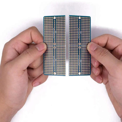 Hands holding two halves of a Four Piece Solderable Breadboard Shield With Split Design PCB Prototyping Board Double Sided Tinned Gold Plated Holes.