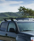 Heavy Duty Universal Roof Rack Bar Cover In Matte Black Aerodynamic Shell Provides Zero Hassle Fit And Slashes Wind Drag For Pickup Trucks On Weekend Getaways Up To 40 Inches Wide on a dark pickup truck driving through scenic landscape.