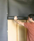 Man applying Premium Mass Loaded Vinyl Soundproofing Rolls Heavy Hitter Noise Blocking Barrier on wall indoors.