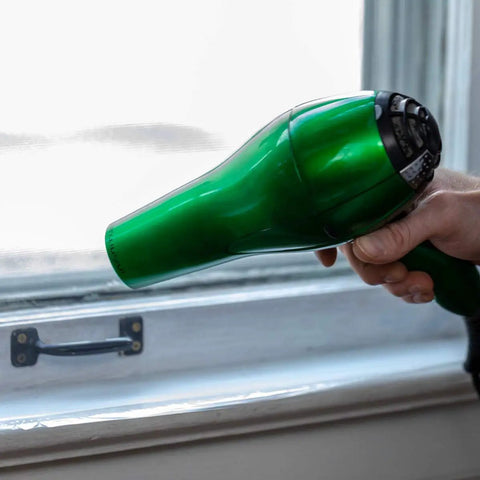 Person using hairdryer on Indoor Three Window Shrink Film Insulator Kit With Crystal Clear Film 62 By 126 Inches Includes 54 Feet Double Sided Tape