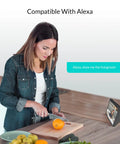 Woman using voice control with Alexa device while preparing food in kitchen, demonstrating Indoor Security Cam 1080p HD WiFi 2.4GHz compatibility.