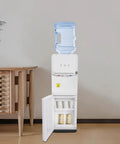 Top Loading Water Cooler For 5 Gallon Bottles With Hot Cold And Warm Water Three Temperature Options And Child Safety Lock Quiet Home Office Dispenser Durable White Construction For Everyday Use next to wooden cabinet.