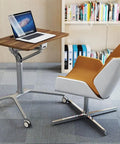 Game Changer Height Adjustable Standing Desk With Silky Gas Lift And Ultra Quiet Lockable Rubber Wheels beside a modern swivel chair.