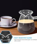 Glass coffee pot with handle on wooden table, alongside white cup and saucer. Close-up of heat-resistant glass feature.