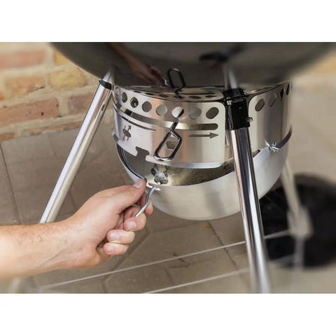 Hand using the One Touch Cleaning System on the Original Kettle Premium Charcoal Grill 22 Inch Black Outdoor BBQ Grill.