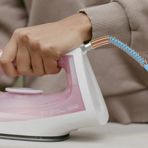 Person using a PTFE High Temperature Steam Hose For Steam Irons High Pressure Tube Lightweight And Durable Steam Line For Ironing Flexible Hose For Garment Care Easy Connect Pro Grade Home Use connected to a pink iron.