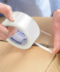 Applying 2 Inch Clear Packing Tape 2.4 Mil Thick 110 Yards Per Roll on a cardboard box, showing adhesive hold and clarity for shipping.