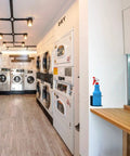 Wall Mounted Spray Bottle Holder Rack For Garage And Home holds a blue spray bottle in a laundry room setup.