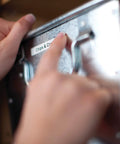 Hand reaching for a labeled metal storage container, showcasing organization using the Rock Solid Compact Handheld Label Printer Featuring Bold Fonts And Live Graphical Display For Nailing Home Office Paperwork And Quick Storage Organization Hustle.