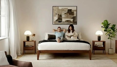 Premium King Solid Wood Bed Frame With Classic Japanese Joinery And Reinforced Wooden Slats For Rock Solid Support That Ditches The Box Spring Requirement While Providing Hassle Free Assembly For Your Cozy Bedroom Vibe In Rich Walnut with a couple relaxing in a cozy bedroom.