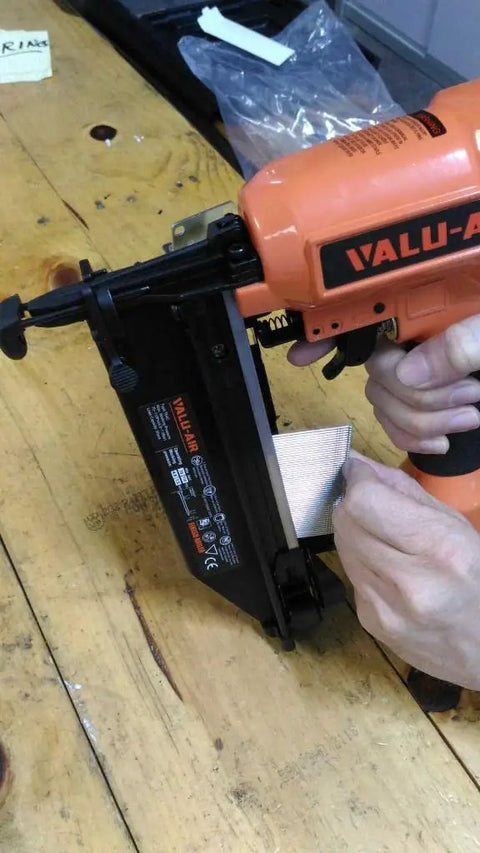 Person using a pneumatic nail gun to load Pro Grade Galvanized Finish Nails 16 Gauge 1 Inch Straight Head Built Tough For Pneumatic Or Cordless Nailer Guns Solid 2500 Count Box For Fine Woodworking And Trim Installations.