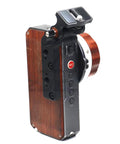 Side view of HangTon monitor bracket mounted on Tilta Nucleus-M hand unit; black metal clamp, wooden grip, REC button visible.