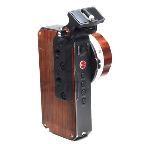 Side view of HangTon monitor bracket mounted on Tilta Nucleus-M hand unit; black metal clamp, wooden grip, REC button visible.