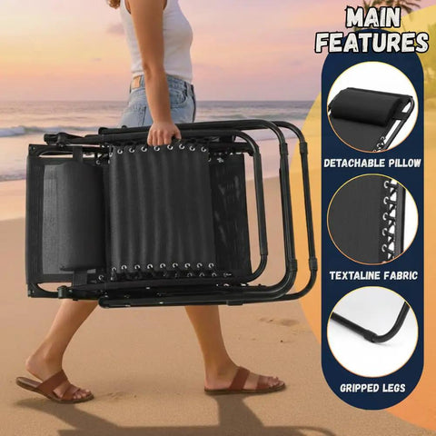Person carrying folded Zero Gravity Lounge Chair For Poolside And Patio Adjustable Reclining Steel Mesh Folding Recliner With Pillow And Cup Tray Outdoor Camping Beach Chair Black on a beach; close-ups of pillow, fabric, legs shown.