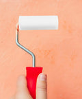 Straight Up Quality Mini Sponge Paint Roller Covers, No Worries Low Lint Sleeves, held with red handle, against peach wall.