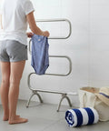 Person using Classic 37.5-Inch Nickel Heated Towel Warmer Rack with 4 Bars, freestanding, drying swimsuit in bathroom.