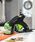 Cordless High Temperature Glue Gun 60W with standby base for craft projects shown with decorative items on table.