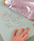 Foil Quill pen starter kit with pink foil applied to floral line art on blue card; hand visible