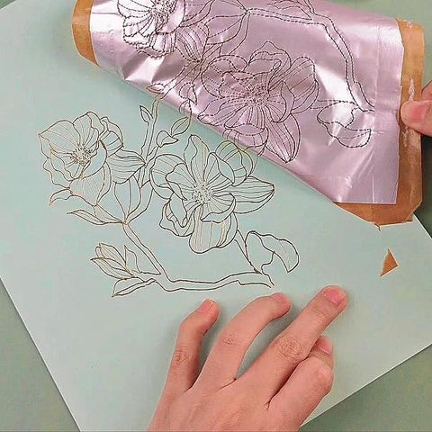 Foil Quill pen starter kit with pink foil applied to floral line art on blue card; hand visible
