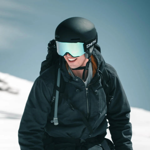 Hydration tube accessory for outdoors; skier in black jacket wearing helmet and mirrored goggles in snow
