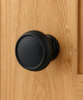 Close-up of a matte black cabinet knob installed on a wooden cabinet door, 10 Pack Matte Black Cabinet Knobs 1-1/4 Inch Modern Zinc Alloy Hardware