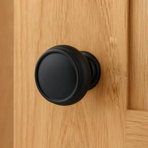 Close-up of a matte black cabinet knob installed on a wooden cabinet door, 10 Pack Matte Black Cabinet Knobs 1-1/4 Inch Modern Zinc Alloy Hardware