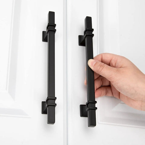 Person installing 25 Pack 5 Inch Matte Black Cabinet Pulls Zinc Alloy Dresser Handles on white cabinet doors.