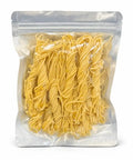 Clear vacuum-sealed package of yellow dry ramen noodles standing upright, showing strands through transparent plastic packaging.
