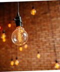 Close-up of a hanging light bulb with glowing filament in a brick-walled room, focus on 20 Pcs Black Ul Twist Lamp Turn Knobs Replacement.