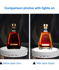 Motorized 360 Degree Rotating Display Stand With Remote Control And Seven Color Led Lights For Jewelry Photography And Collectibles Black 32 Cm Turntable displaying a liquor bottle in dim and bright light.