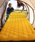Yellow inflatable air mattress inside a tent entrance with people sitting outside, designed for camping comfort