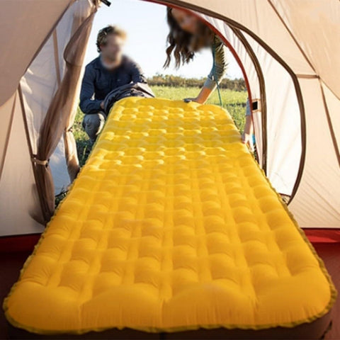 Yellow inflatable air mattress inside a tent entrance with people sitting outside, designed for camping comfort