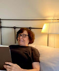 Elderly woman reading in bed under Over-The-Bed Reading Light Two Pack With Soft Fabric Shade Easy On Off Pull Cord Bedside Headboard Lamp For Reading In Bed Cozy Eye-Friendly Book Light For Knitting Puzzles And Chill Nights.