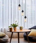 Three Light Industrial Pendant Light With Glass Shade Matte Black Finish Adjustable Height hanging over a table.