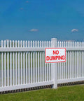 Heavy Duty Aluminum No Dumping Signs Two Pack on a white fence warning against illegal waste disposal outdoors.