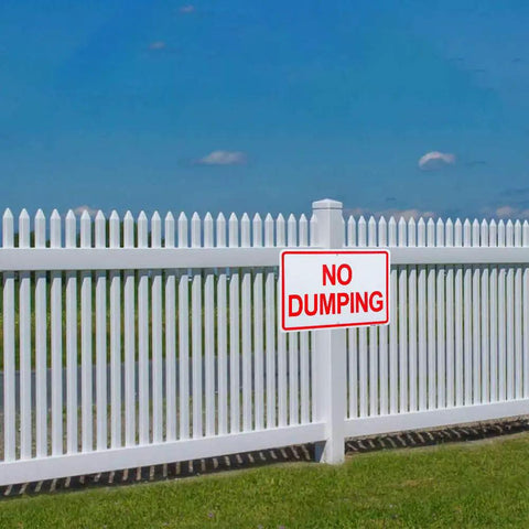 Heavy Duty Aluminum No Dumping Signs Two Pack on a white fence warning against illegal waste disposal outdoors.