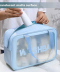 Person placing an item into a blue Go To Travel Toiletry Bag For Women And Men, Matte Translucent Organizer With Handy Handle, Waterproof PVC Case.